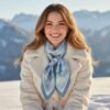 Model smiling in soft sunlight wearing SoieVia™ The Swirling Mist silk scarf with snowy Alps behind — 18 mm silk twill in misty grey and ivory tones, symbol of calm, clarity, and inner balance.