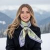 Smiling model wearing SoieVia™ Snowfield Light silk scarf against sparkling Alpine snowfields — 18 mm silk twill in luminous white and crystal tones, symbol of joy and winter elegance.